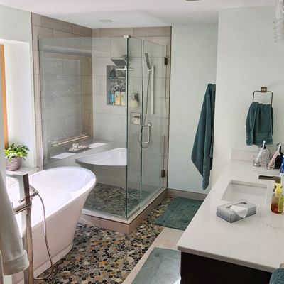 Bathroom remodel featuring a bathtub, custom shower, stone tile, and vanity.